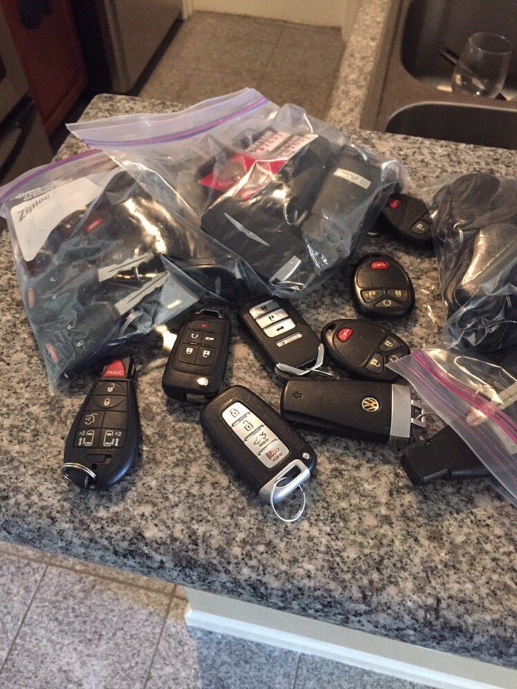 A bag and counter full of assorted car key fobs and remote keys
