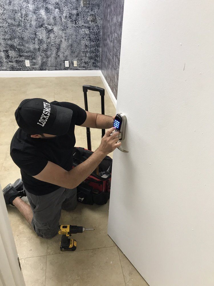 A locksmith installing a keypad lock on a wall beside a rolling tool bag