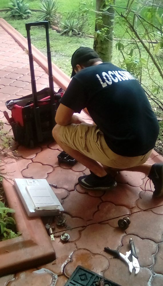 A locksmith kneeling beside a rolling tool bag at an entry while working on a lock