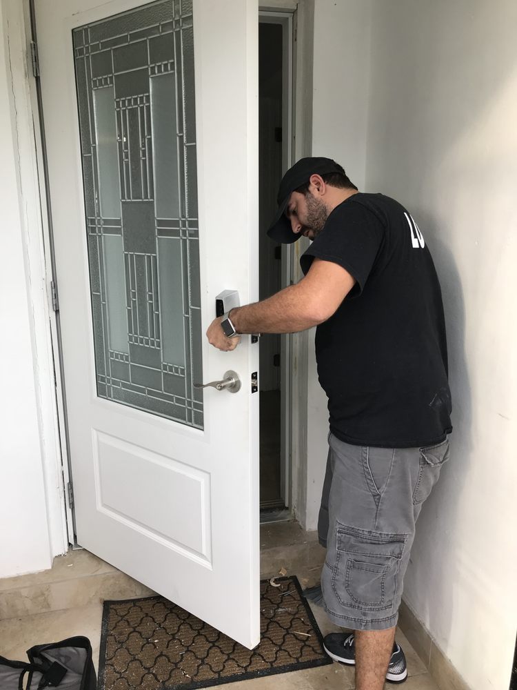A locksmith working on the lock of a white front door with a glass panel
